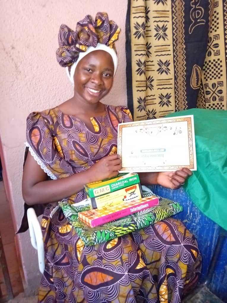 Smiling young woman sat with gifts on her lap and holding up a certificate of graduation